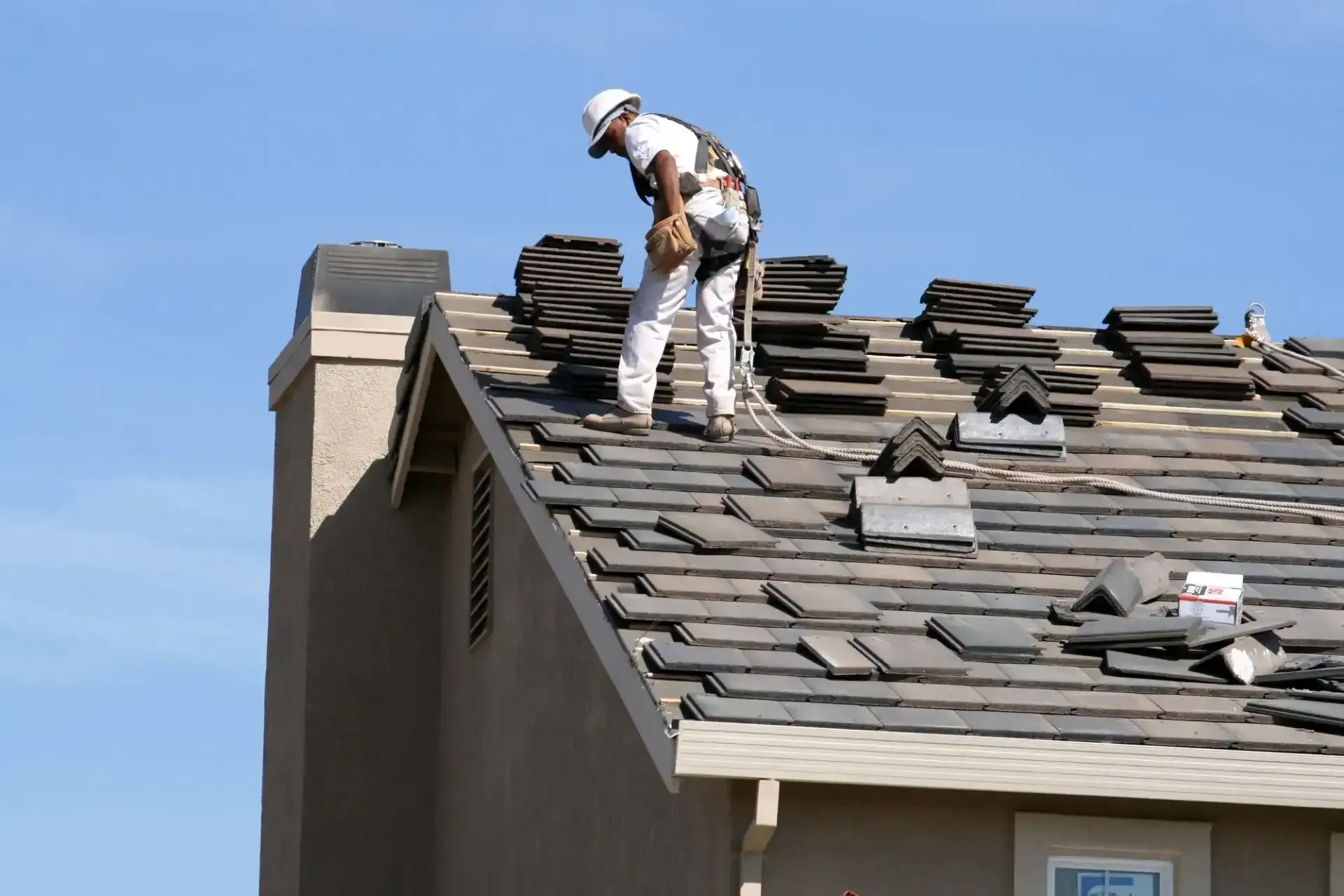 Roofer on a sloped roof, working with tiles under a clear blue sky.