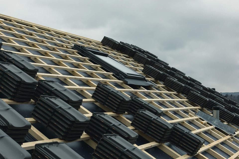 Roof under construction with black tiles and wooden frame.