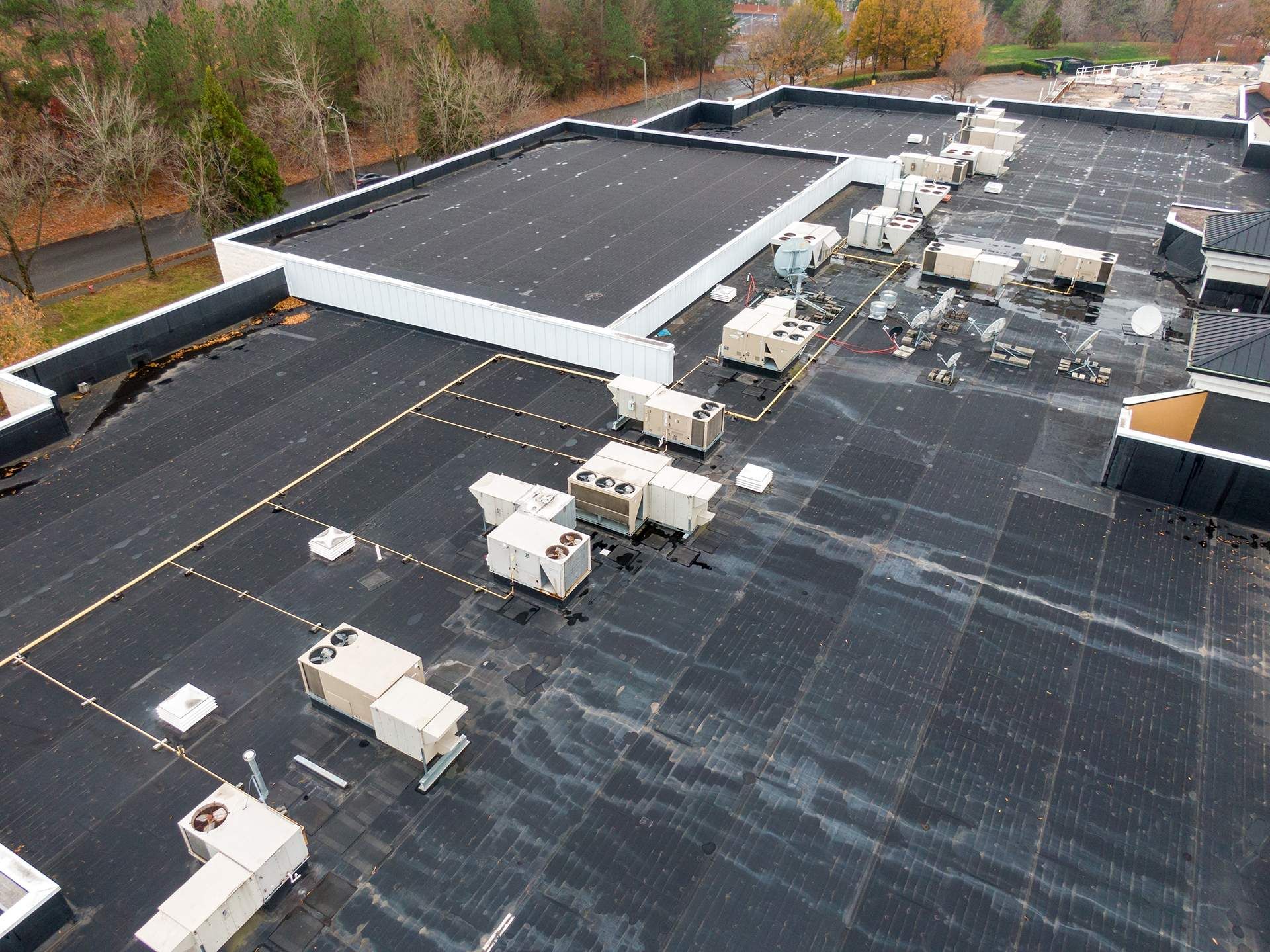 Overhead view of a flat commercial roof with HVAC units. Black roof, white trim, and trees in the background.