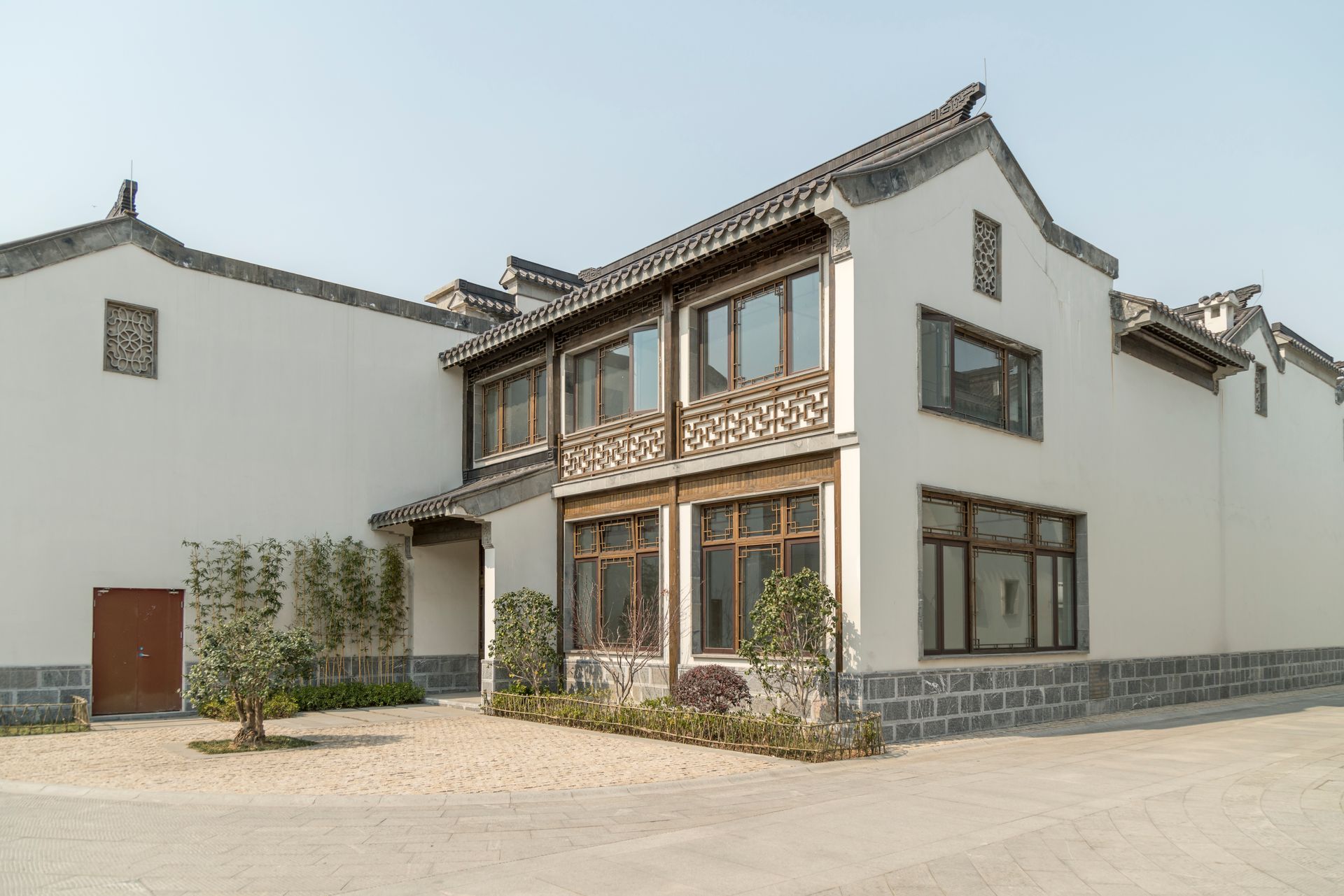 Two-story white building with gray tiled roof and brown framed windows, in a courtyard on a sunny day.