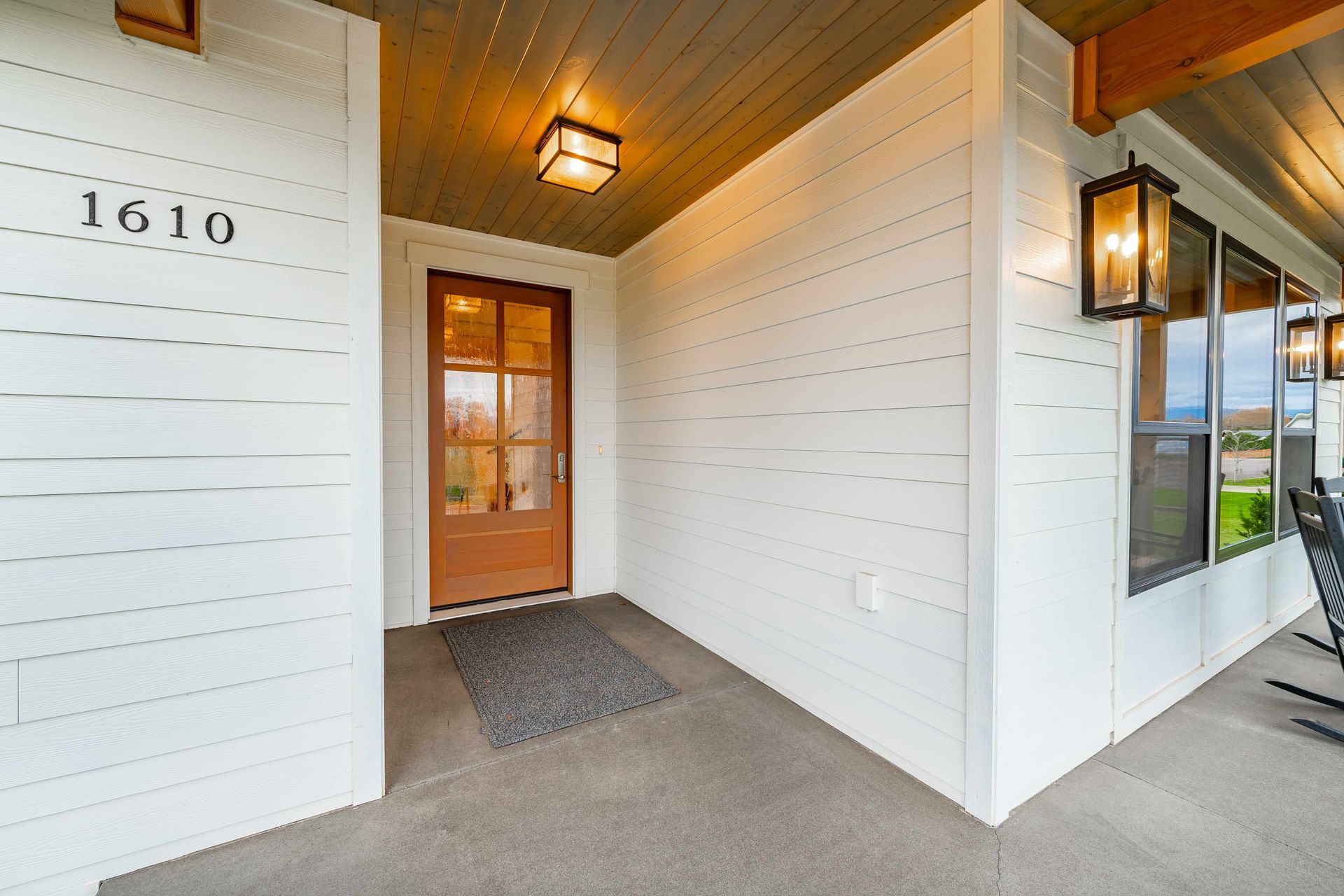 Entryway of a modern house with a brown door, white siding, and porch with windows.