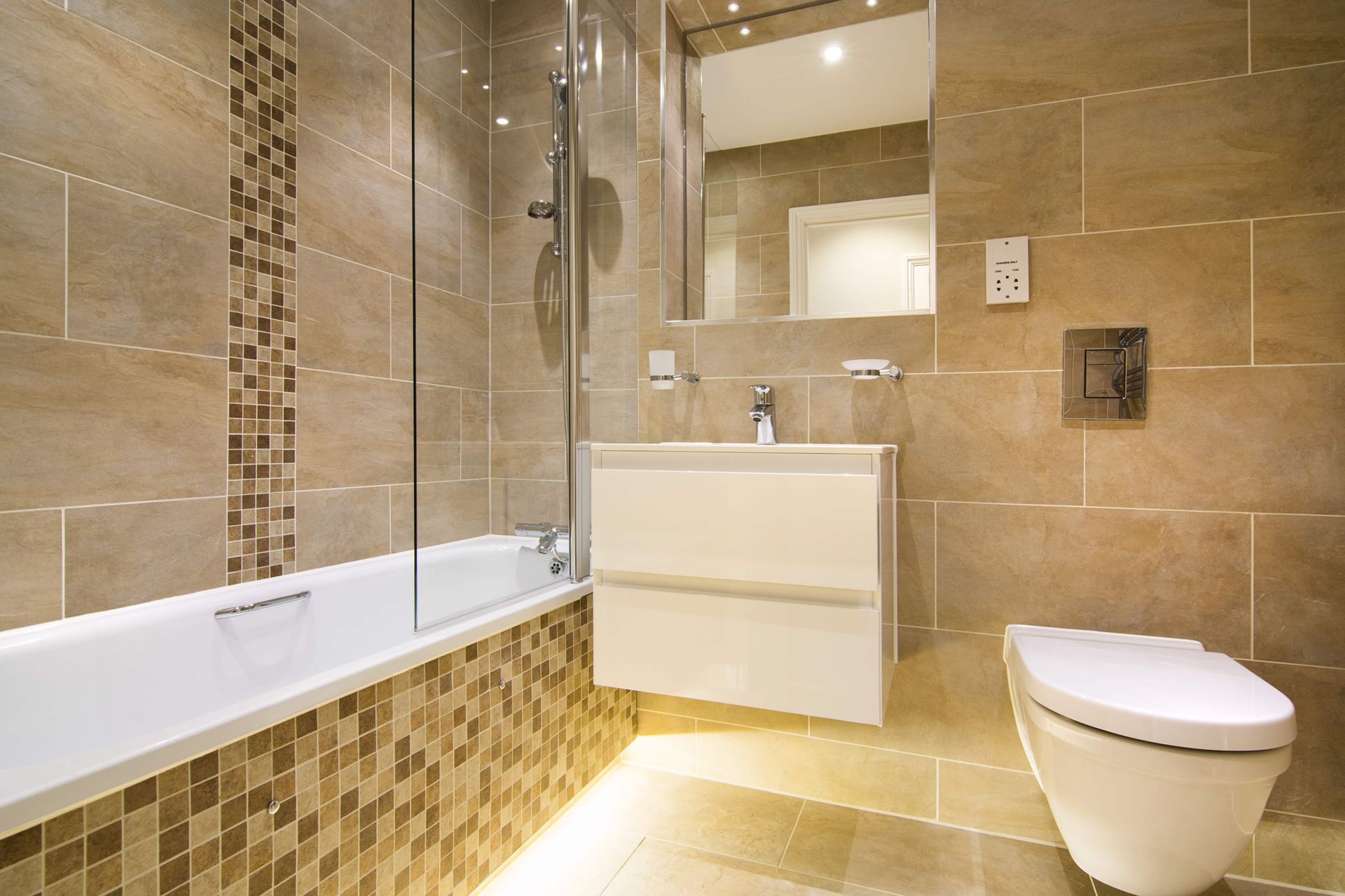 Modern bathroom with beige tiles, glass shower, floating vanity, and toilet.