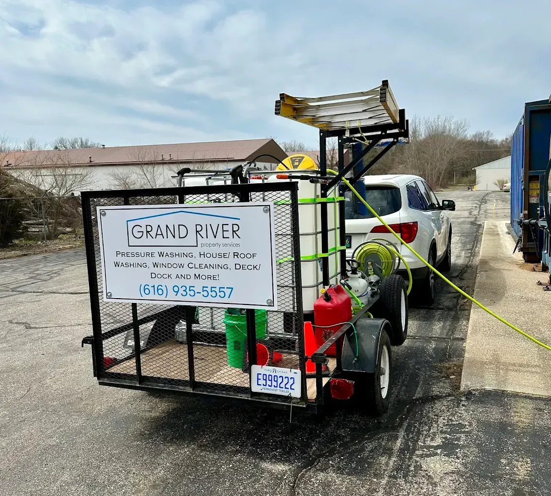 A white SUV towing a trailer with pressure washing equipment; a sign reads
