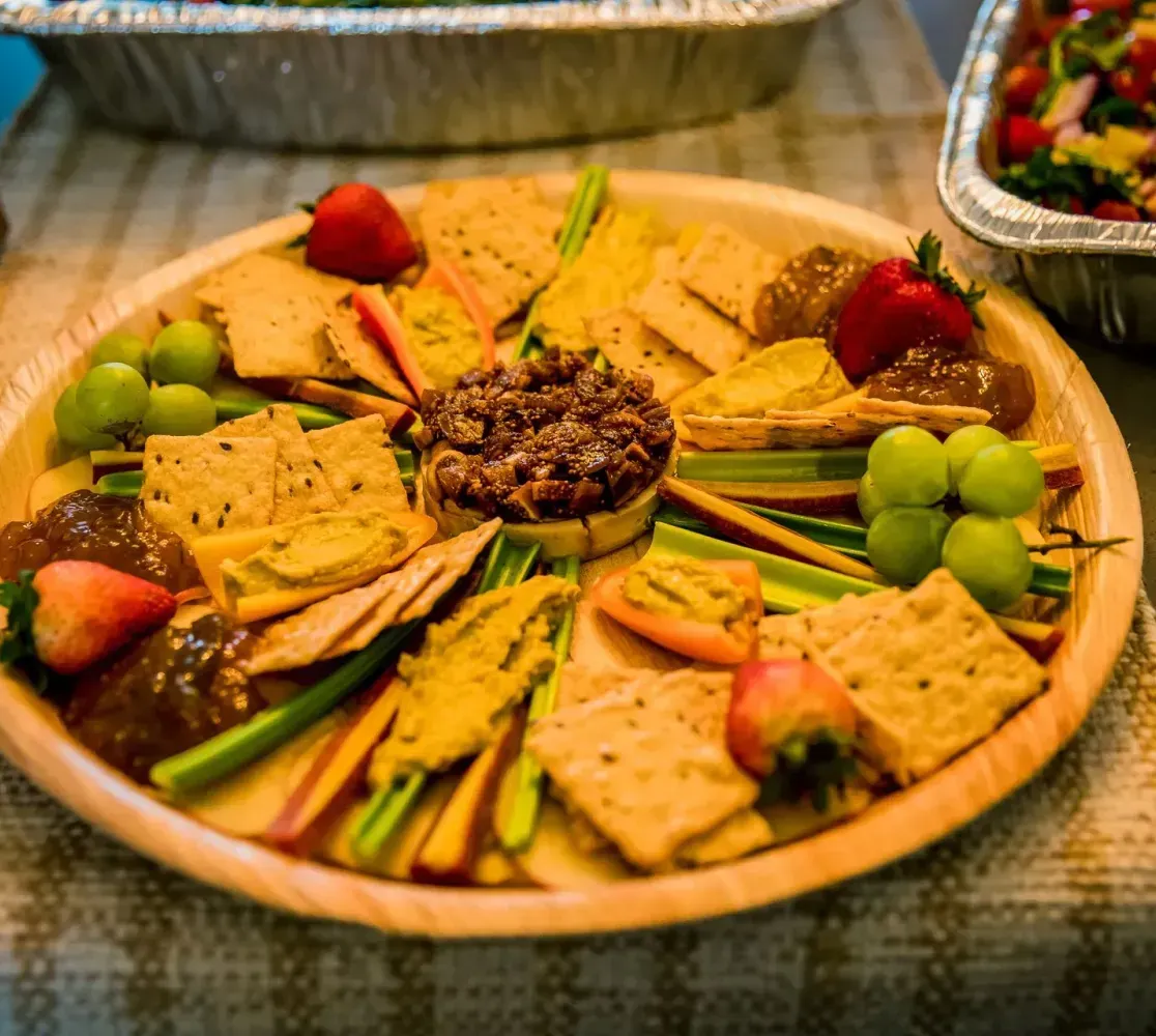 Assorted crackers, strawberries, grapes, and dip arranged on a round wooden platter