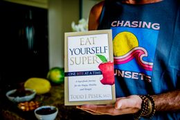 Person holding a book titled “Eat Yourself Super” in front of a blue shirt with colorful graphic.