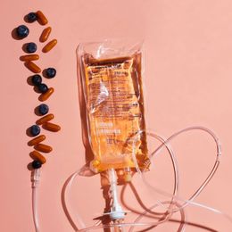 IV bag with amber liquid and tubing beside scattered pills on a pink background