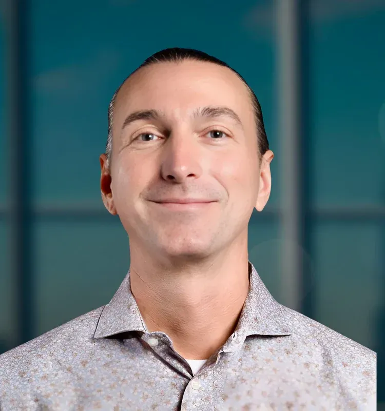 Smiling man in a light patterned shirt against a blurred blue background