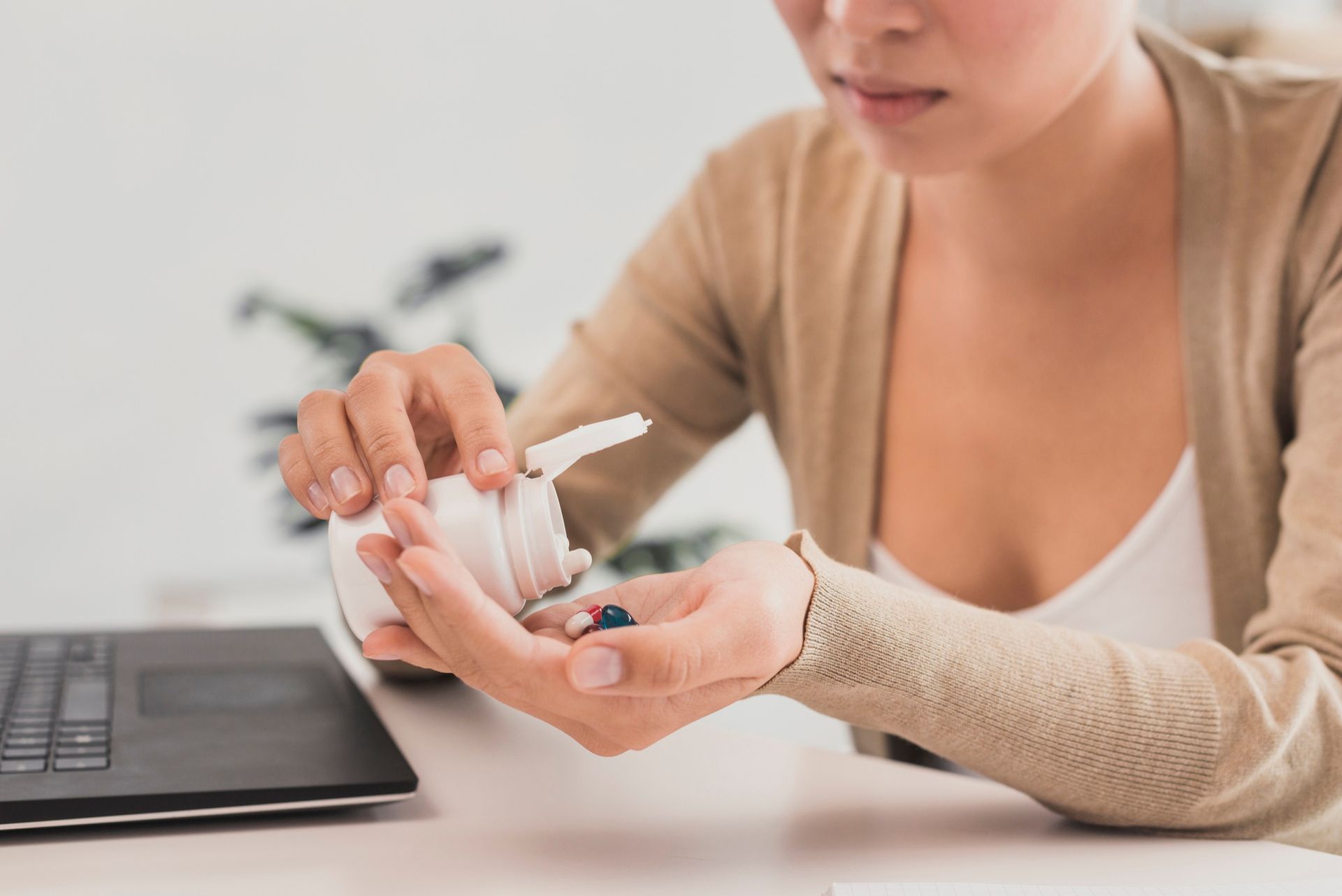 Person holding a white bottle of lotion beside a laptop on a desk