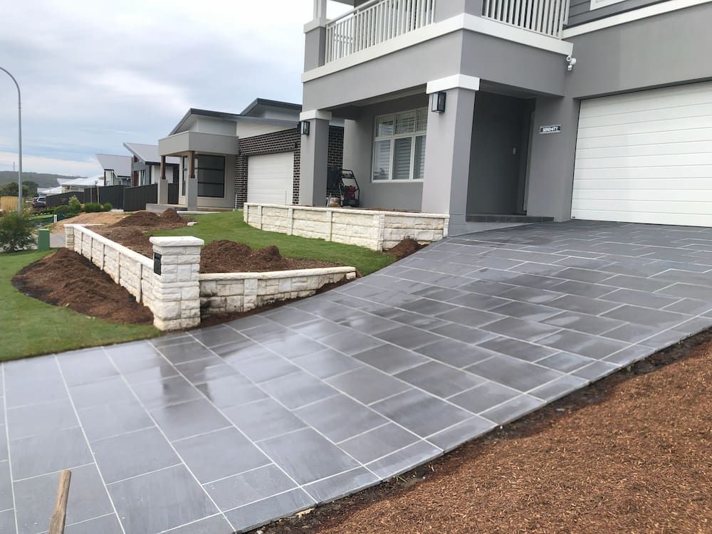 A Driveway Leading to a House With a White Garage Door — Peter Phillips Landscape Design in Bomaderry, NSW