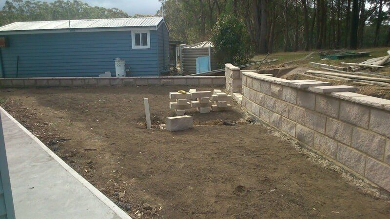 A Brick Wall Is Being Built in Front of A Blue House — Peter Phillips Landscape Design in Kiama, NSW