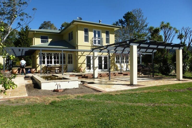 A Large Yellow House with A Pergola in Front of It — Peter Phillips Landscape Design in Sussex Inlet, NSW