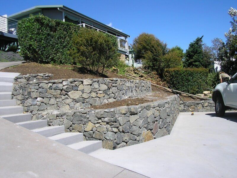A White Car Is Parked in Front of A Stone Wall — Peter Phillips Landscape Design in Bomaderry, NSW