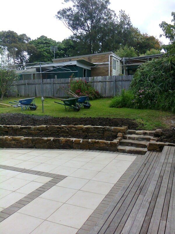 A Wheelbarrow Is Sitting in A Yard Next to A Wooden Deck — Peter Phillips Landscape Design in Bomaderry, NSW