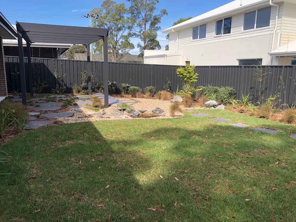 A Backyard With a Lush Green Lawn and a Black Fence — Peter Phillips Landscape Design in Bomaderry, NSW