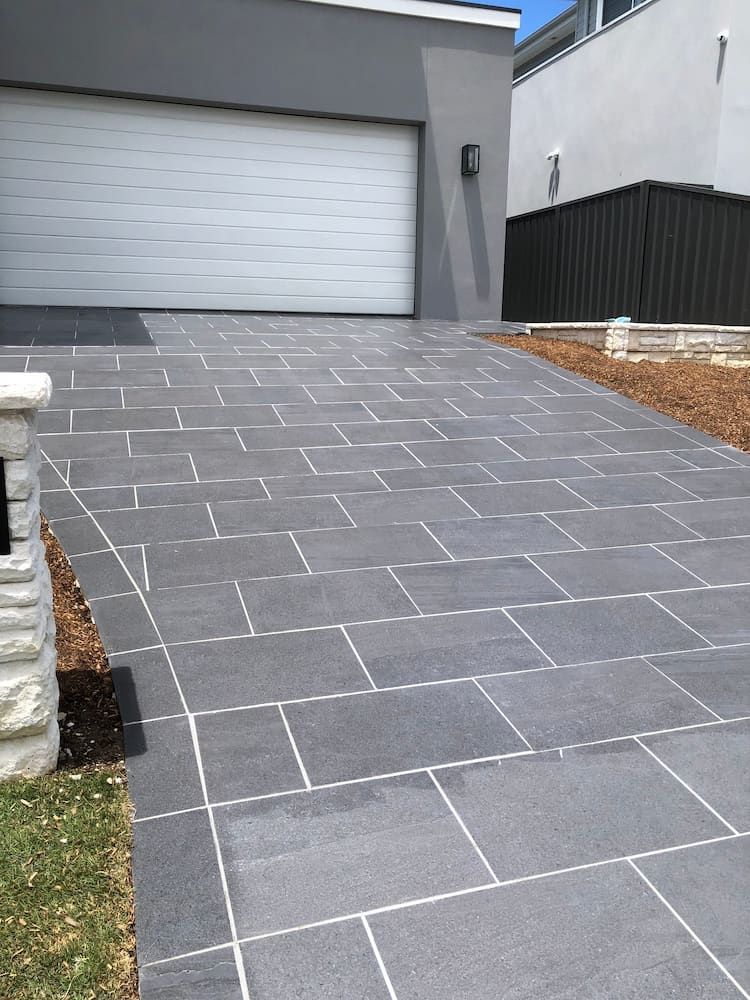 A Brick Driveway Leading to a Garage With a White Garage Door — Peter Phillips Landscape Design in Bomaderry, NSW