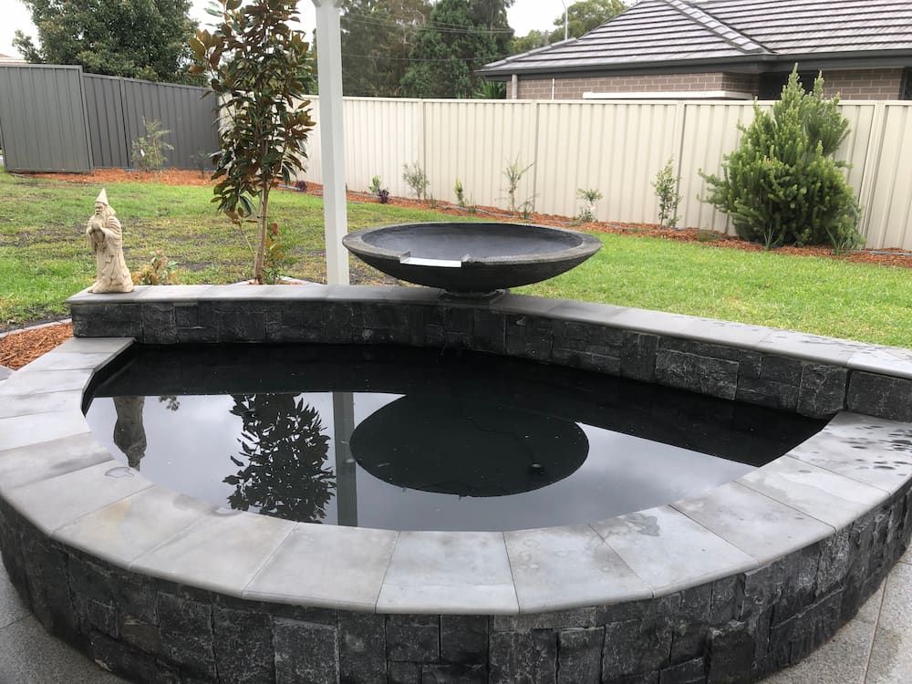 A Large Black Bowl is Sitting in the Middle of a Pond — Peter Phillips Landscape Design in Bomaderry, NSW