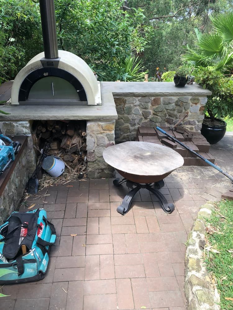 A Pizza Oven is Sitting on Top of a Brick Patio Next to a Fire Pit — Peter Phillips Landscape Design in Bomaderry, NSW