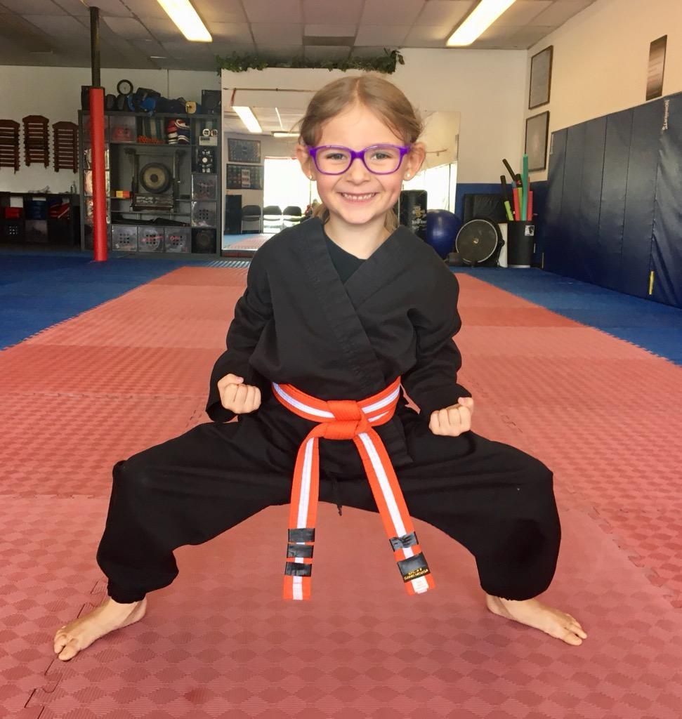 A young girl wearing a black karate uniform and an orange belt