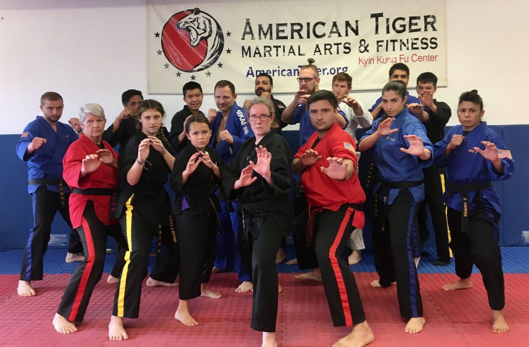 A group of people are posing for a picture in front of a sign that says american tiger martial arts & fitness. Our students understand the benefits of martial arts.