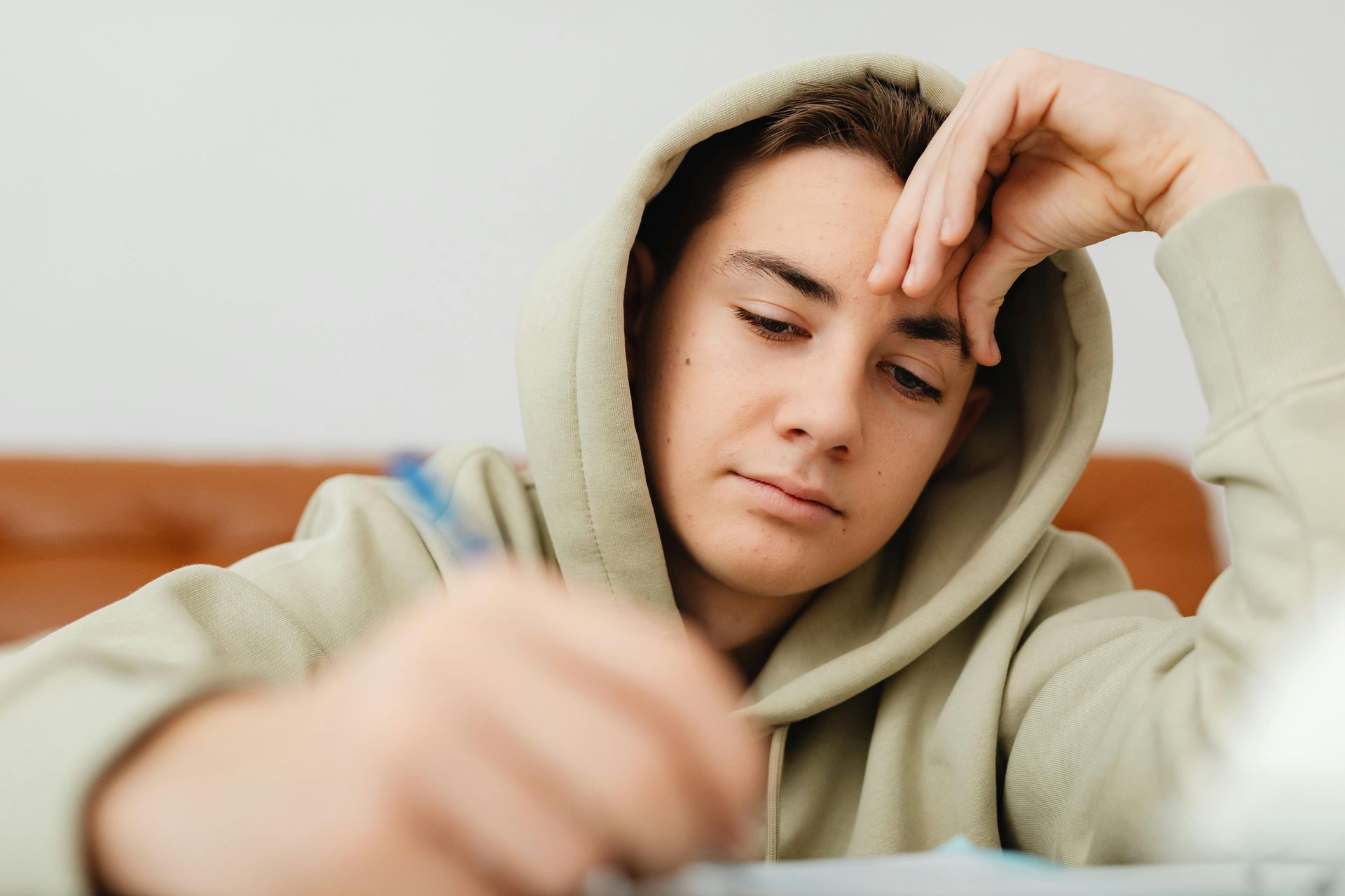 Tired person in a light hoodie resting their head on a hand at a desk