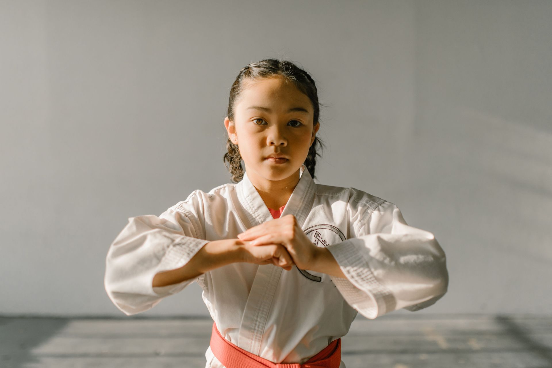 Person in a white martial arts uniform and red belt stands with clasped hands in a studio.