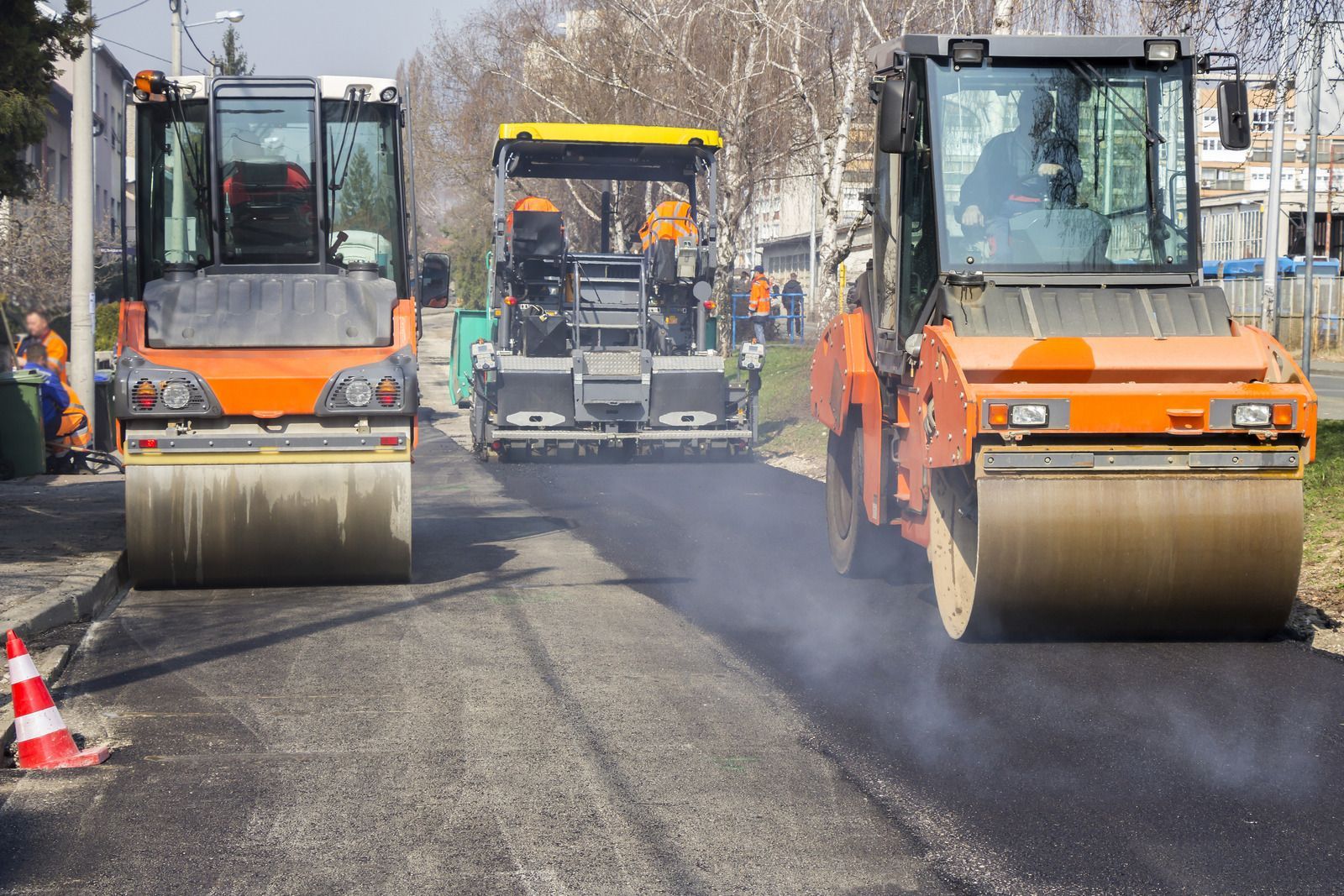 Road paving: Three construction vehicles compacting asphalt on a road, orange and yellow hues.