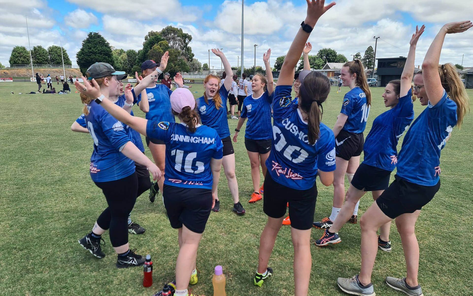 a group of girls are standing in a circle on a field with their arms in the air .