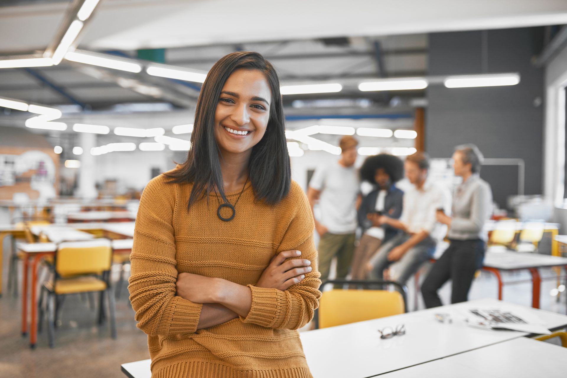 A woman is standing in an office with her arms crossed and smiling.