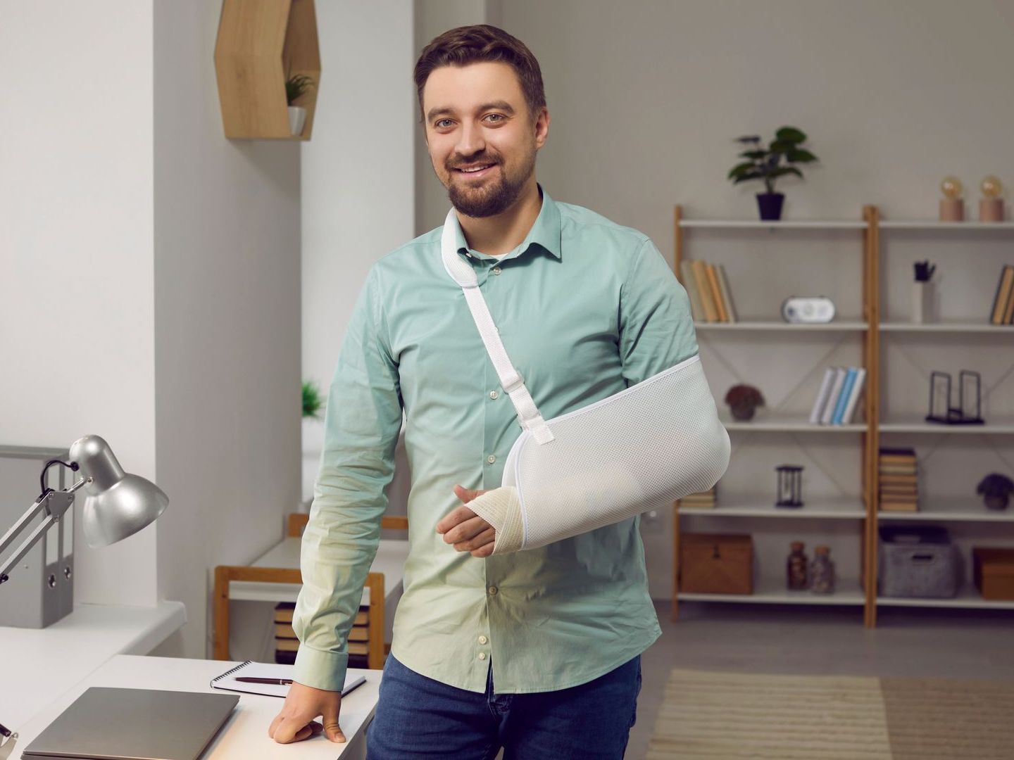 A man with a broken arm in a cast is standing in front of a desk.