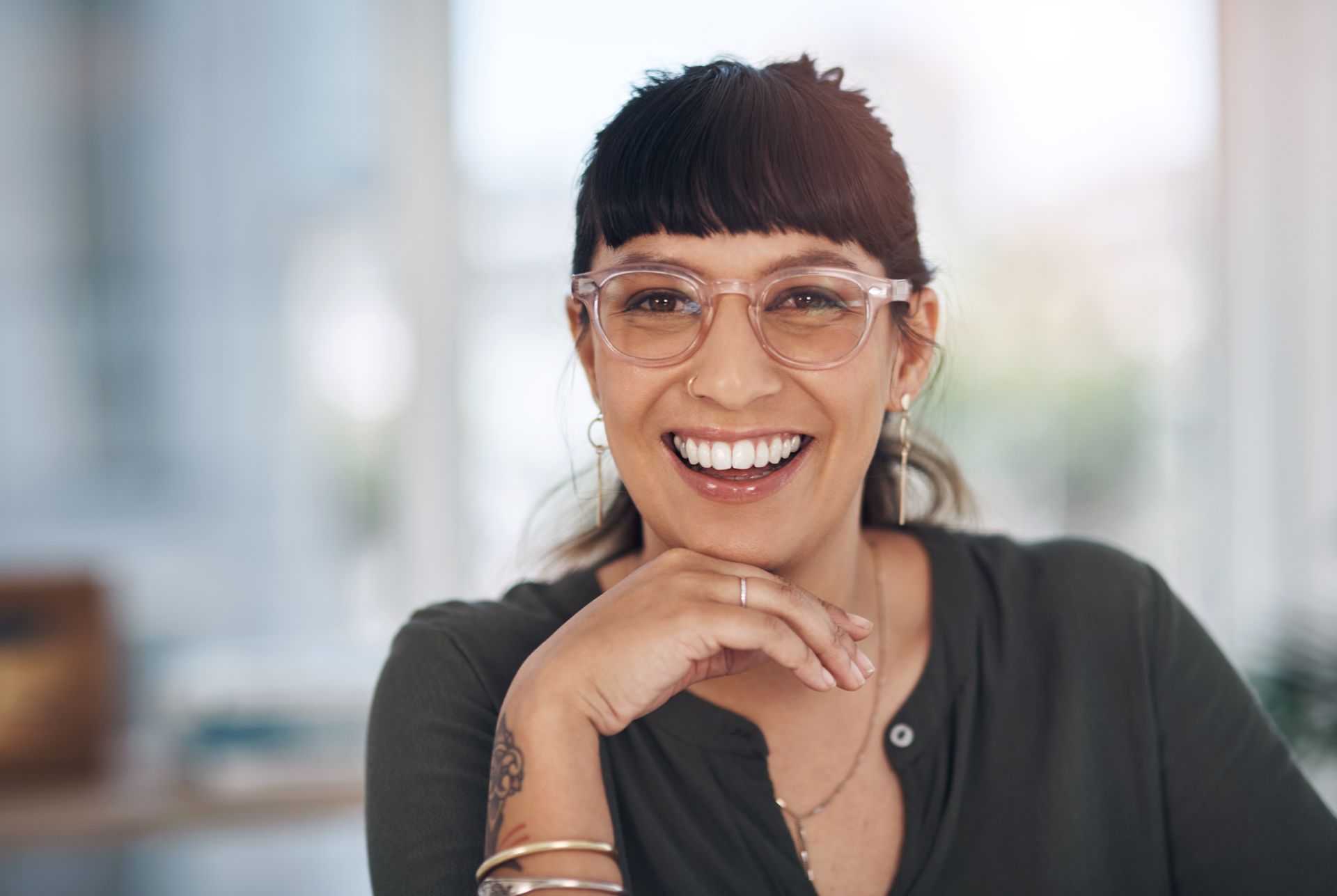 A woman wearing glasses is smiling with her hand on her chin.