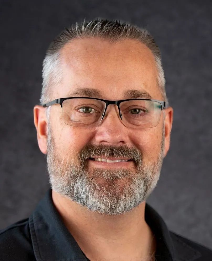 A man with a beard and glasses is smiling for the camera.