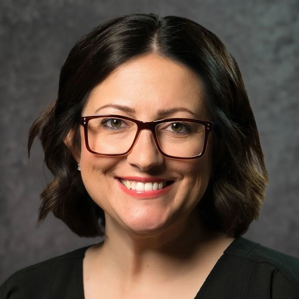 A woman wearing glasses and a black shirt is smiling for the camera.