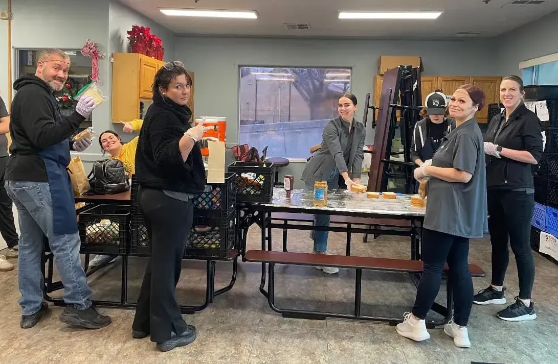 A group of people are standing around a picnic table in a room.