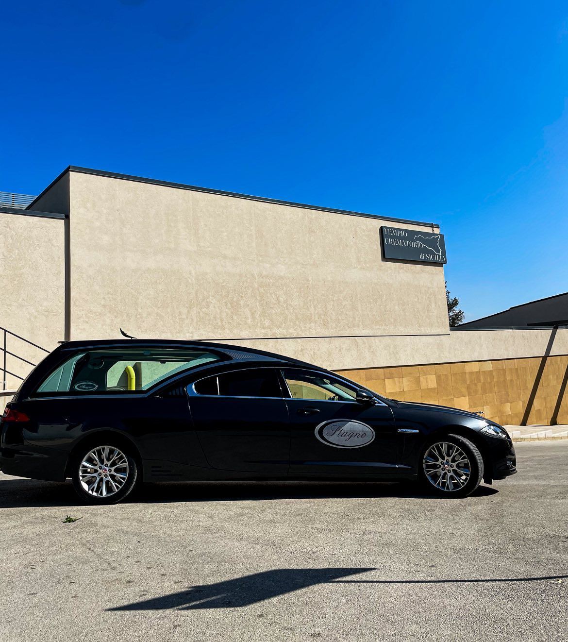 Un carro funebre nero parcheggiato fuori da un edificio in una giornata di sole.