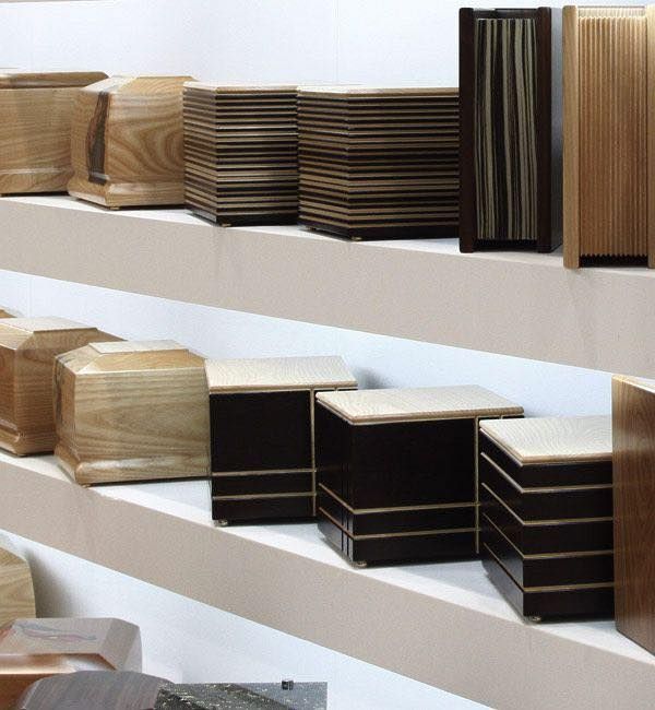Esposizione di varie urne di legno su scaffali a più livelli.
