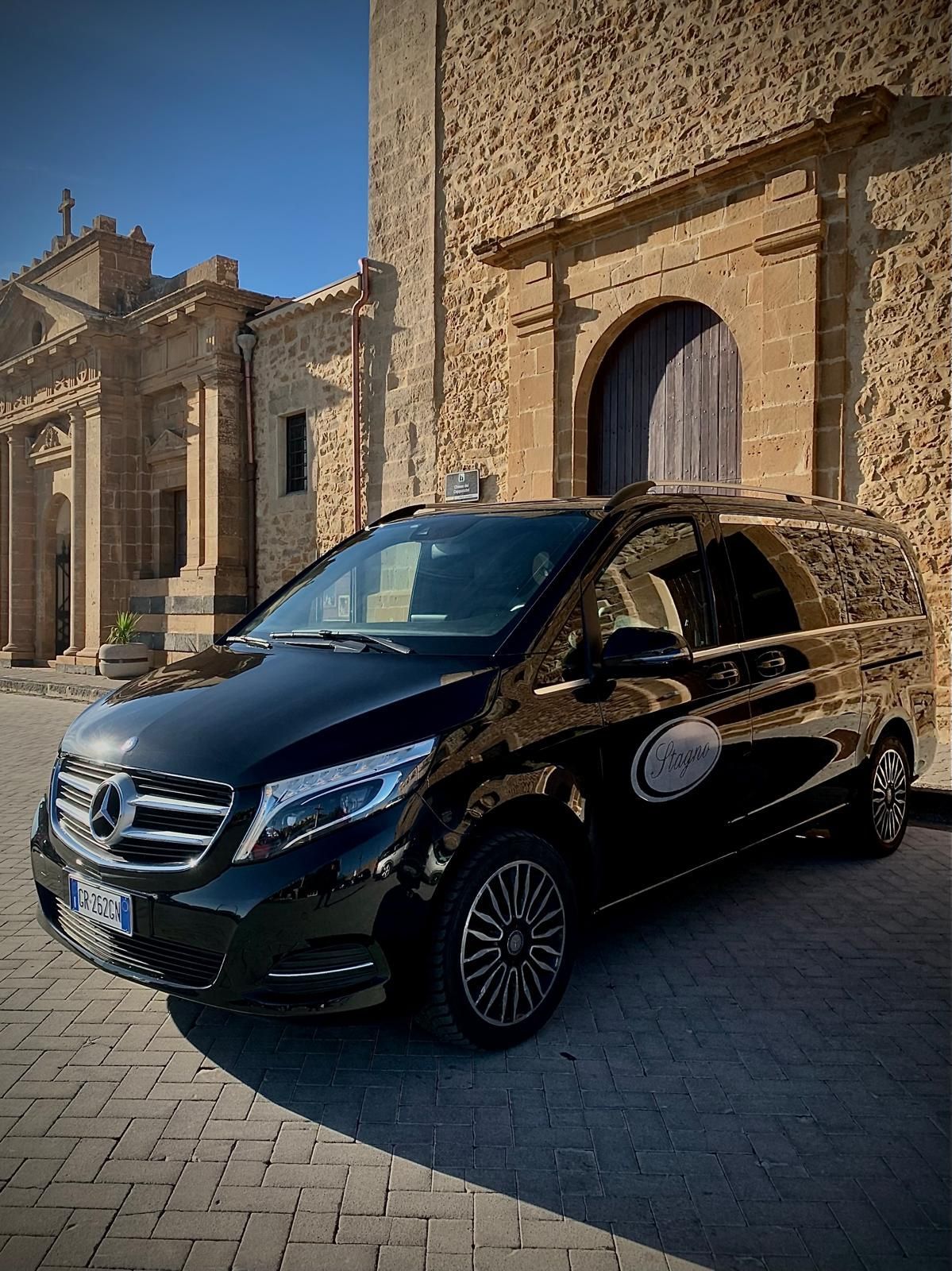 Un minivan Mercedes nero parcheggiato davanti a un edificio in pietra con un portone ad arco.
