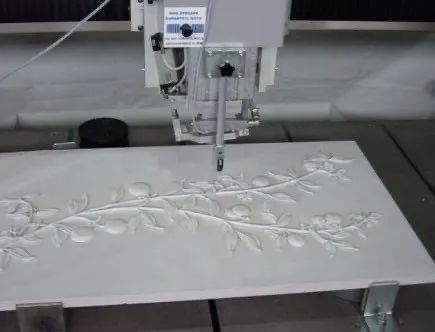 Macchina CNC che intaglia un motivo floreale su una lastra di pietra chiara.