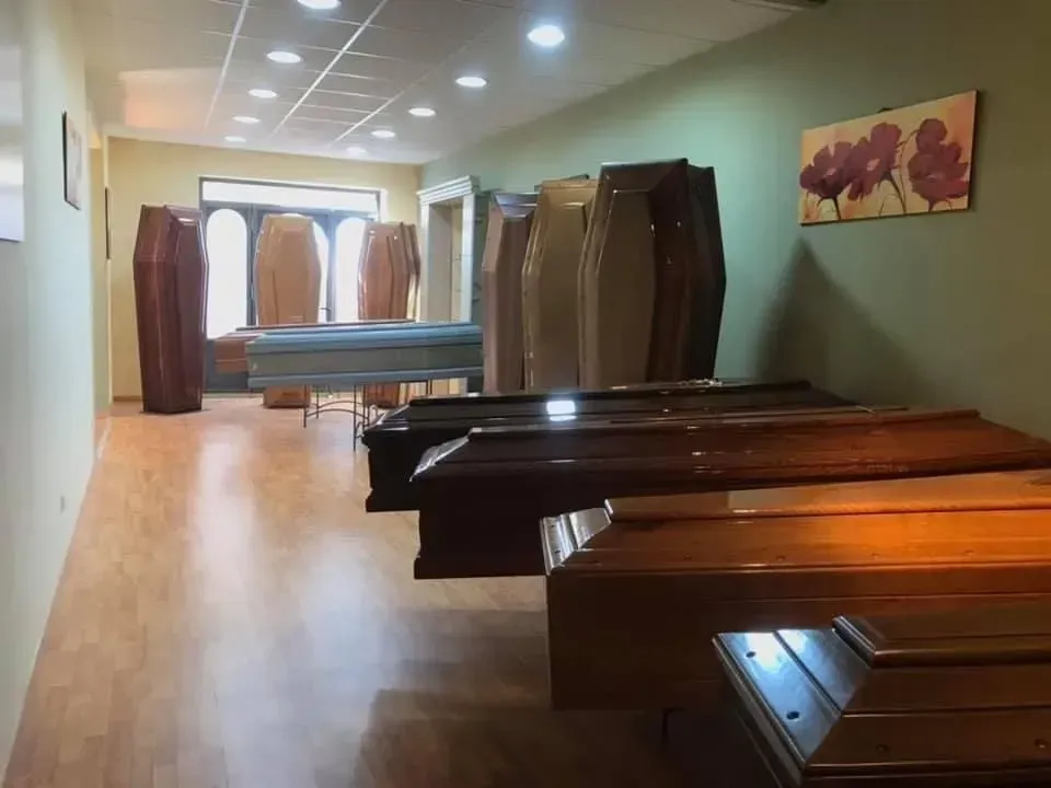 Sala espositiva di un'agenzia di pompe funebri con diverse bare in esposizione; pavimenti in legno e pareti verdi.