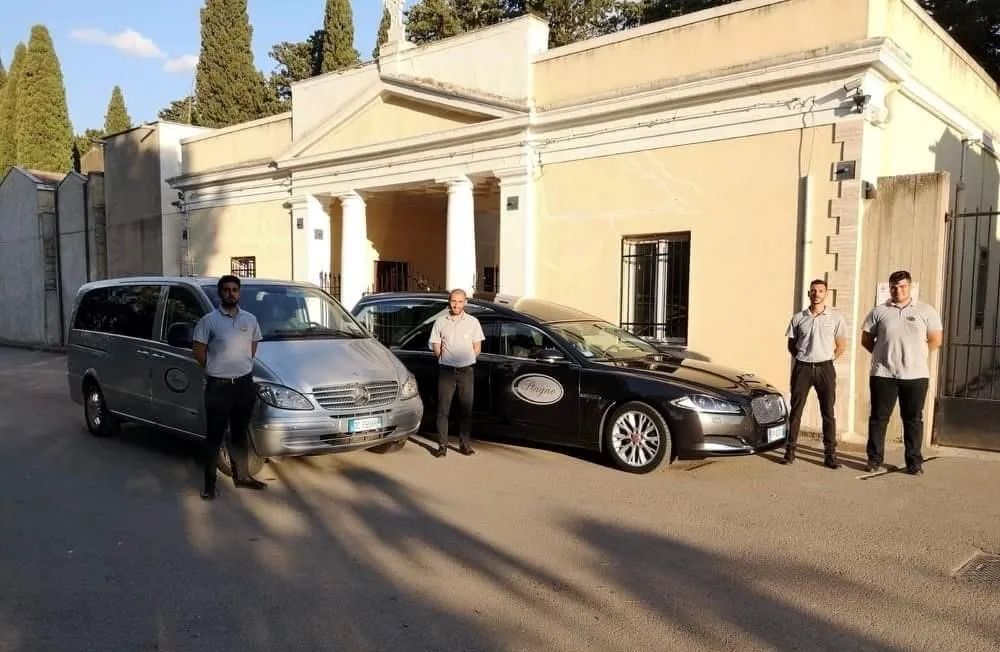 Un gruppo di uomini in piedi accanto a un furgone e un'auto di fronte a un edificio.