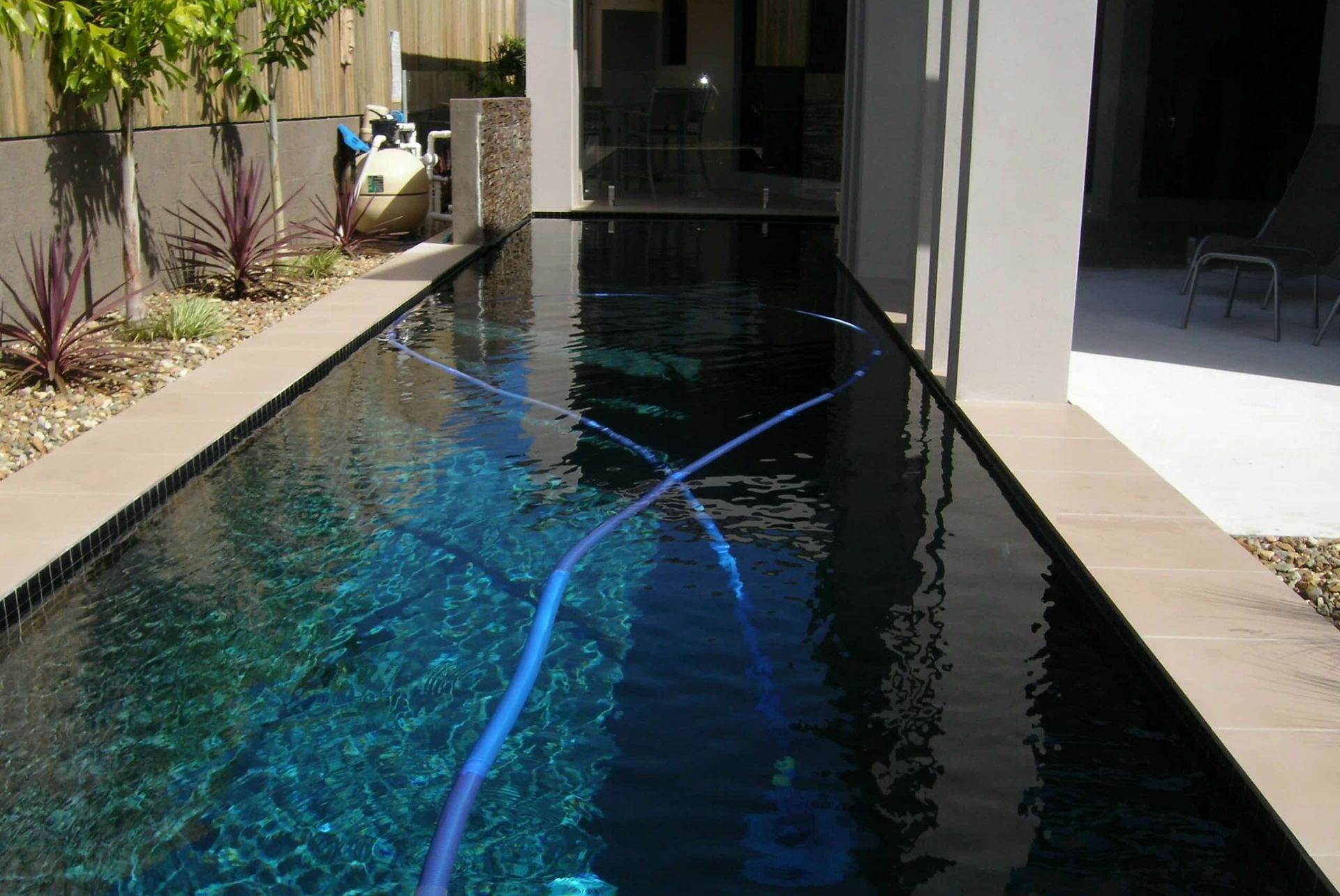 Long, rectangular pool with blue cleaner hose. Water reflects dark sky — Mad Pool Interiors and Renovations in Baringa, QLD