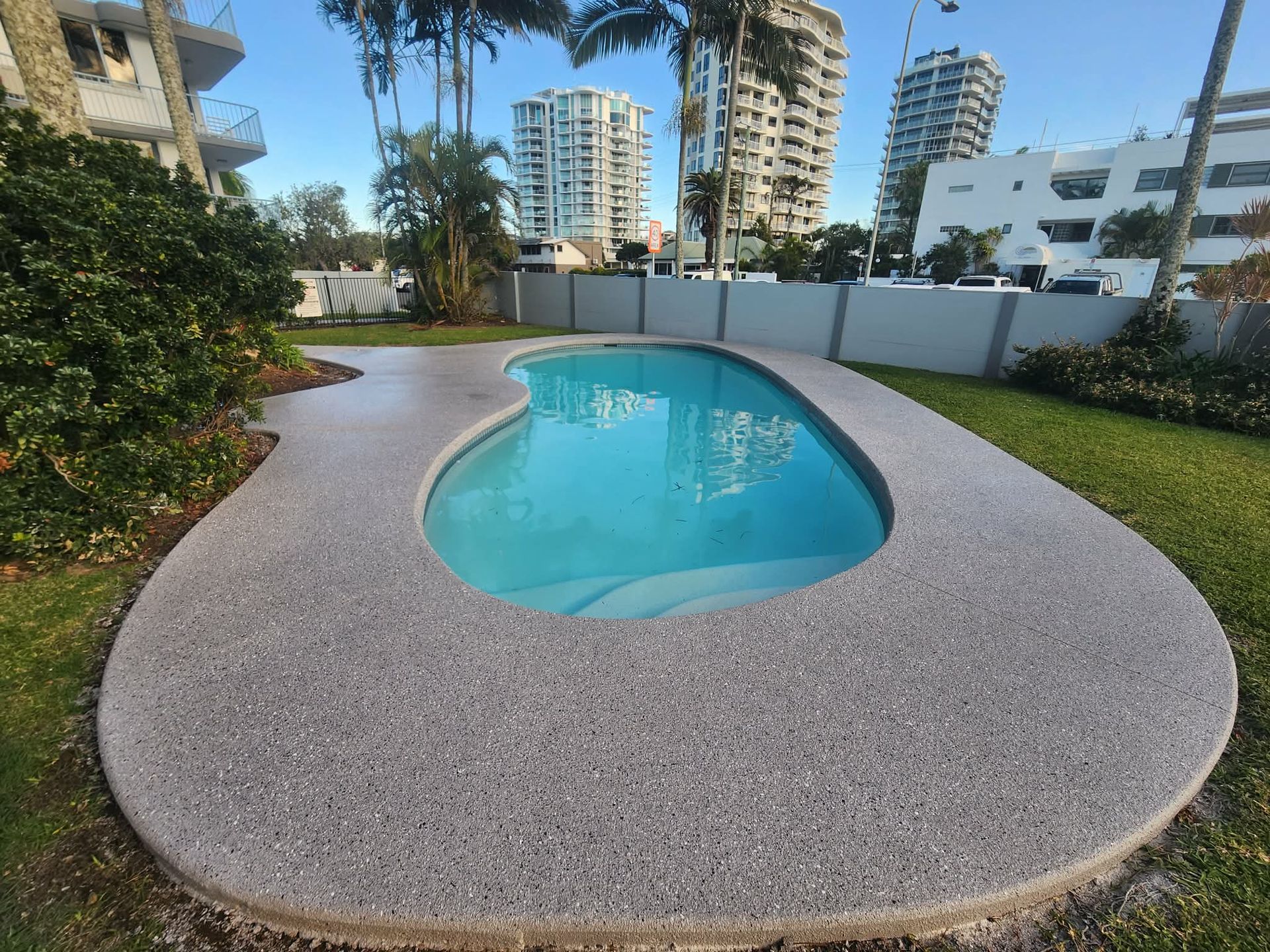 Curved Outdoor Swimming Pool Surrounded by A Gray Deck and Grass — Mad Pool Interiors and Renovations in Baringa, QLD