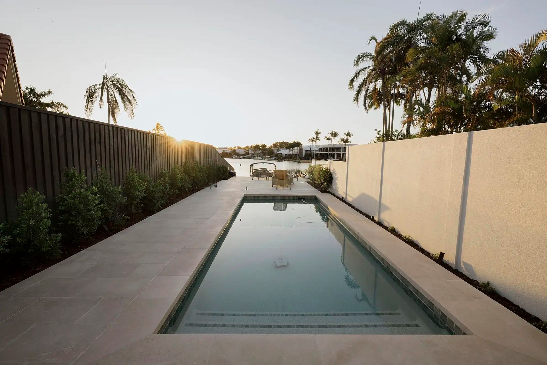 Backyard with A Long Pool, Patio Walls, and Palm Trees at Sunset — Mad Pool Interiors and Renovations in Baringa, QLD