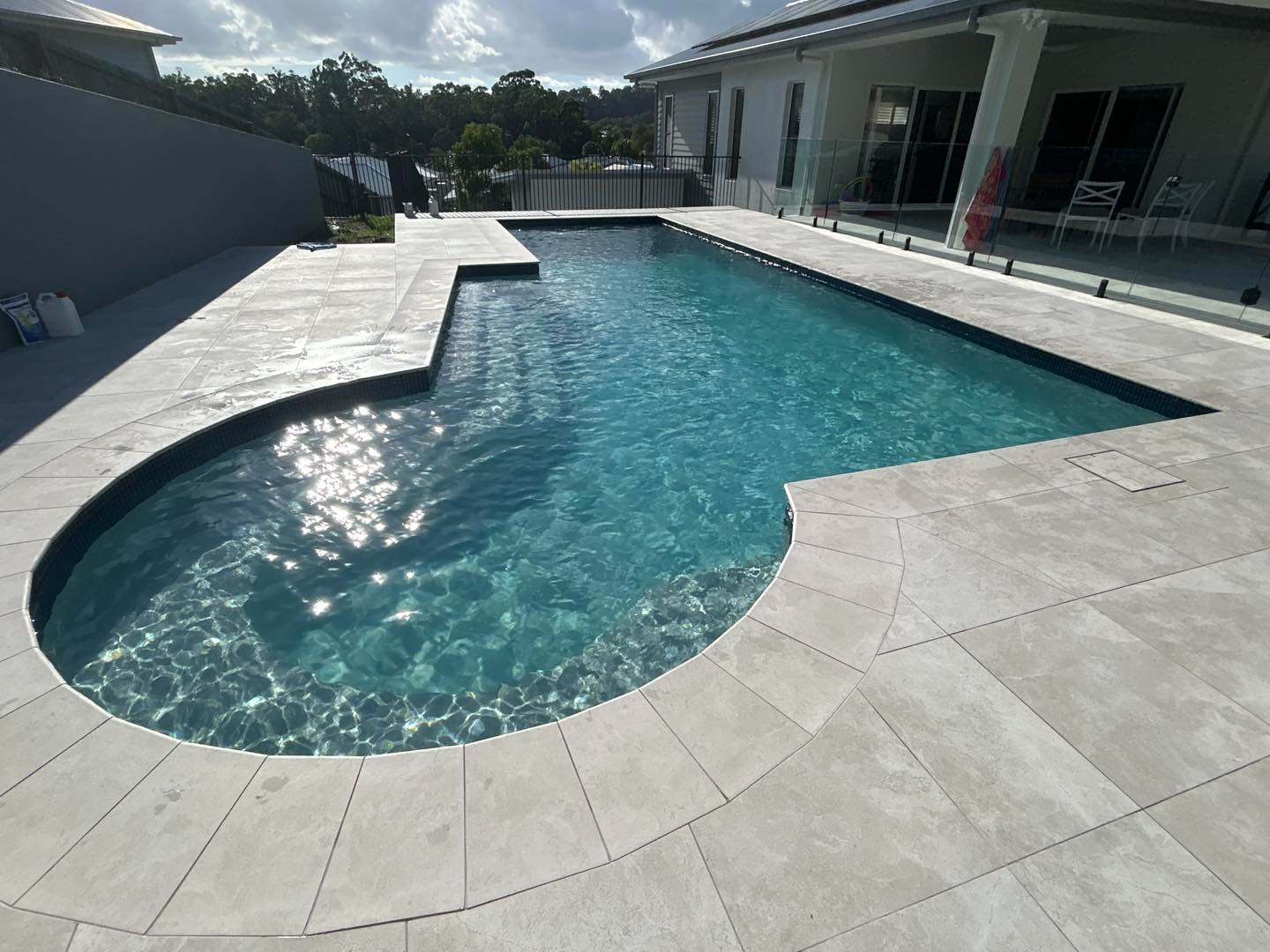 Curved Backyard Swimming Pool With Light Stone Decking — Mad Pool Interiors and Renovations in Baringa, QLD