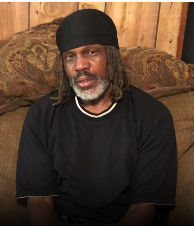 A man wearing a black shirt and a headband sits on a couch