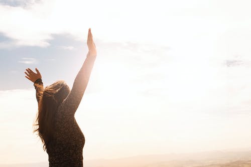 A woman is standing on top of a hill with her arms in the air.