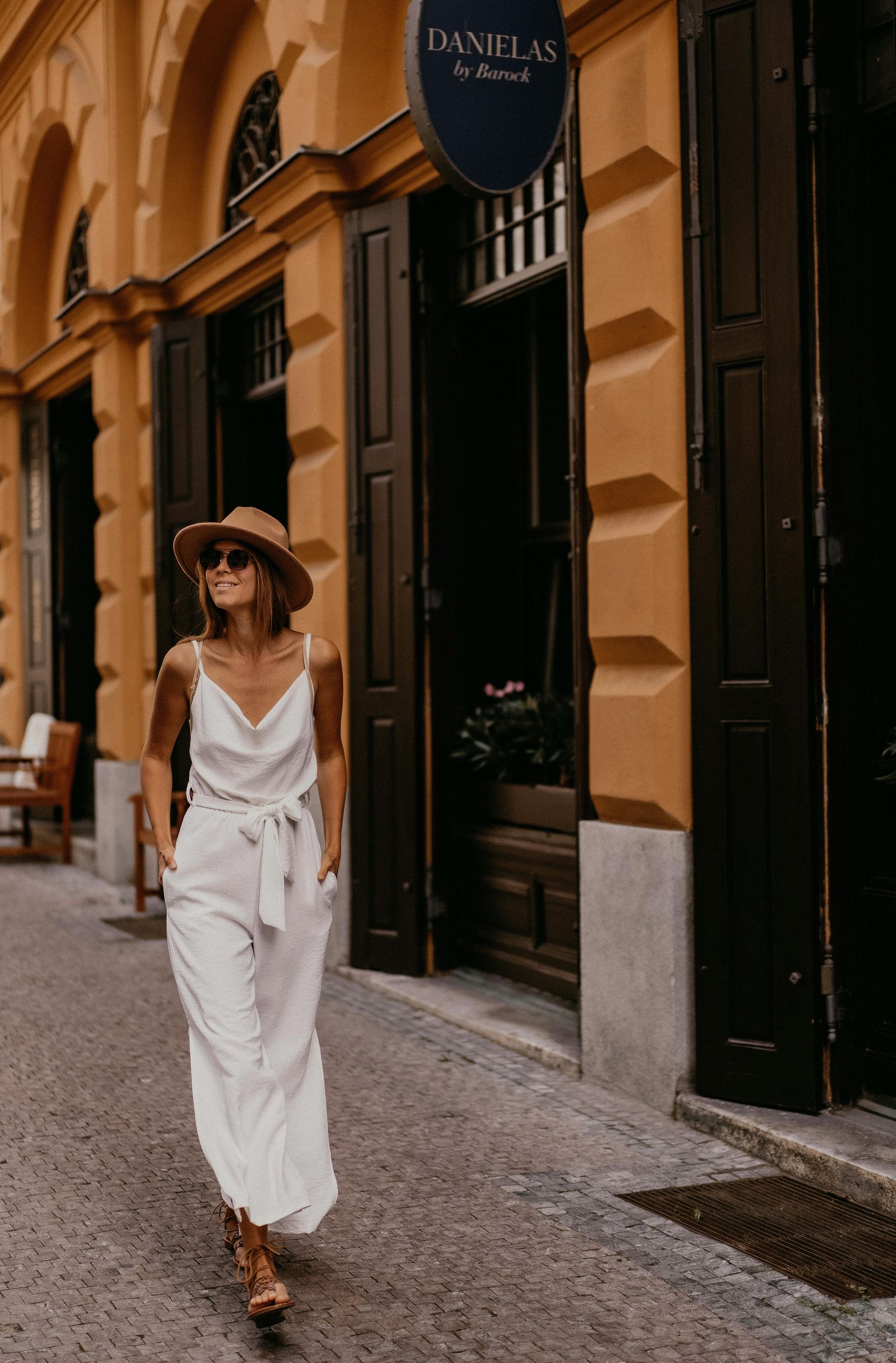 A woman in a white jumpsuit and hat is walking down the street.