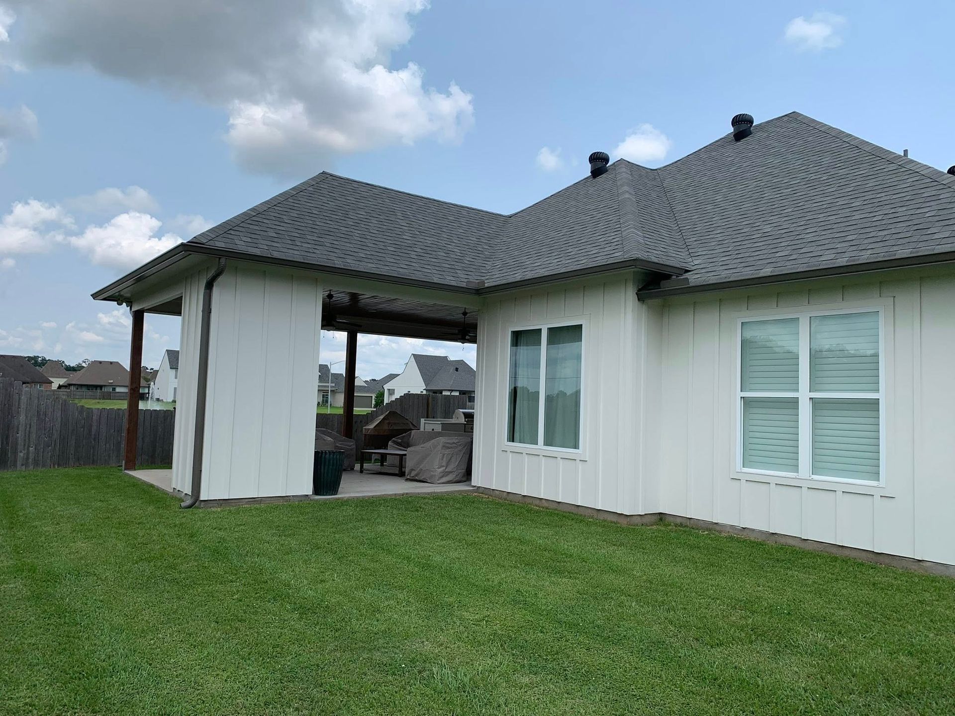 Backyard of a white house with gray roof and green lawn under a partly cloudy sky