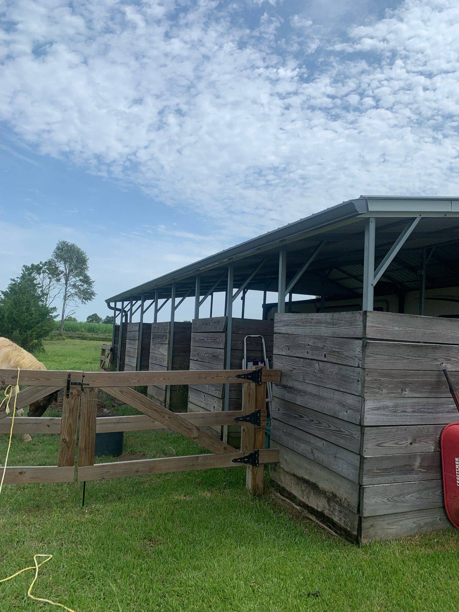 Wooden farm shed with fenced gate and grassy yard under a cloudy sky