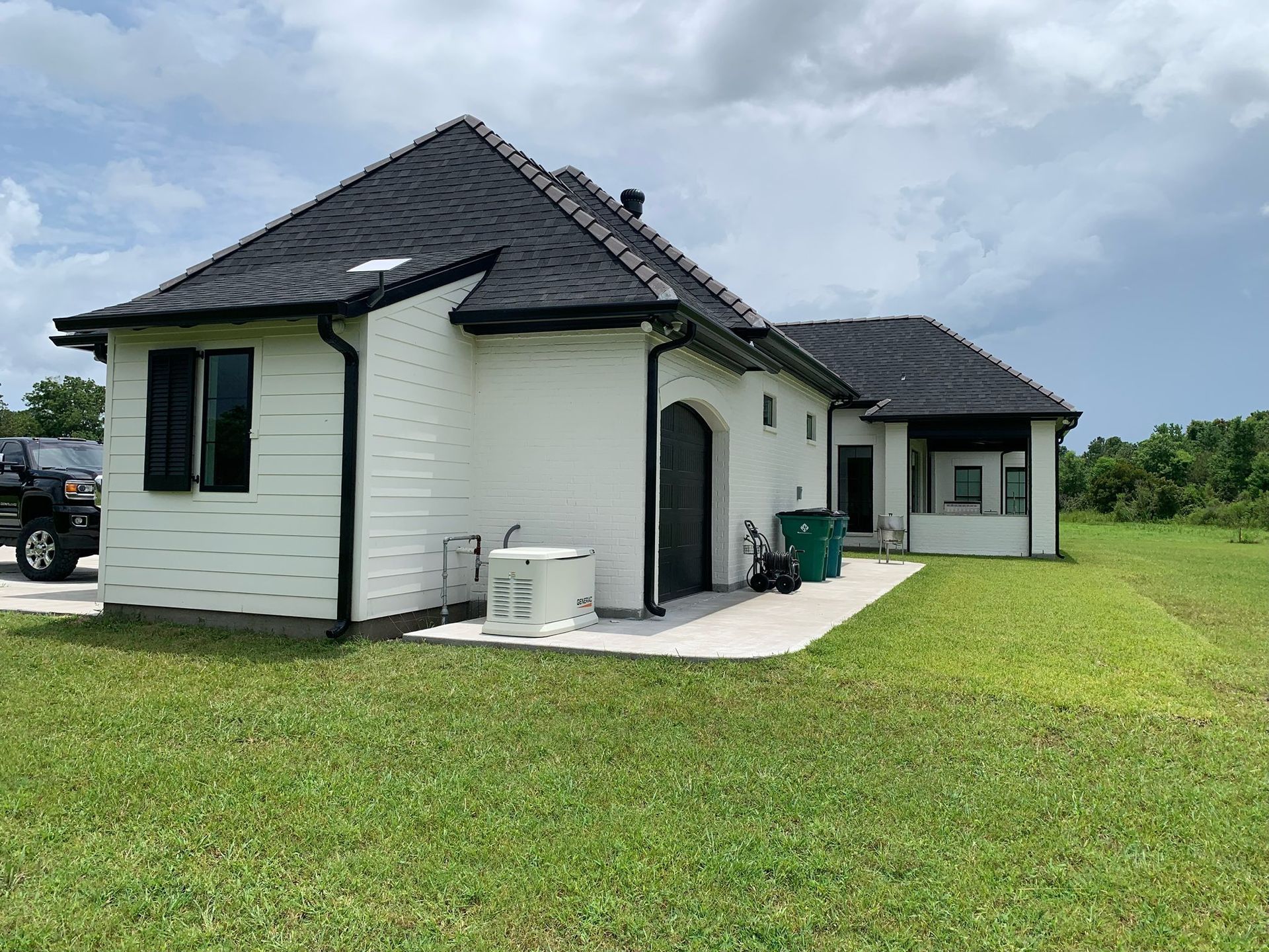 Single-story white house with dark roof and green lawn under a cloudy sky