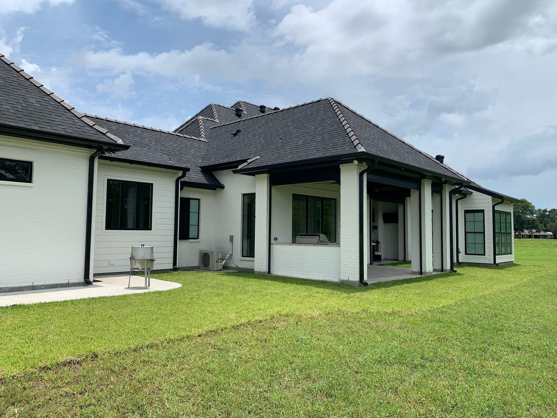 Modern white house with dark roof and green lawn under a cloudy sky